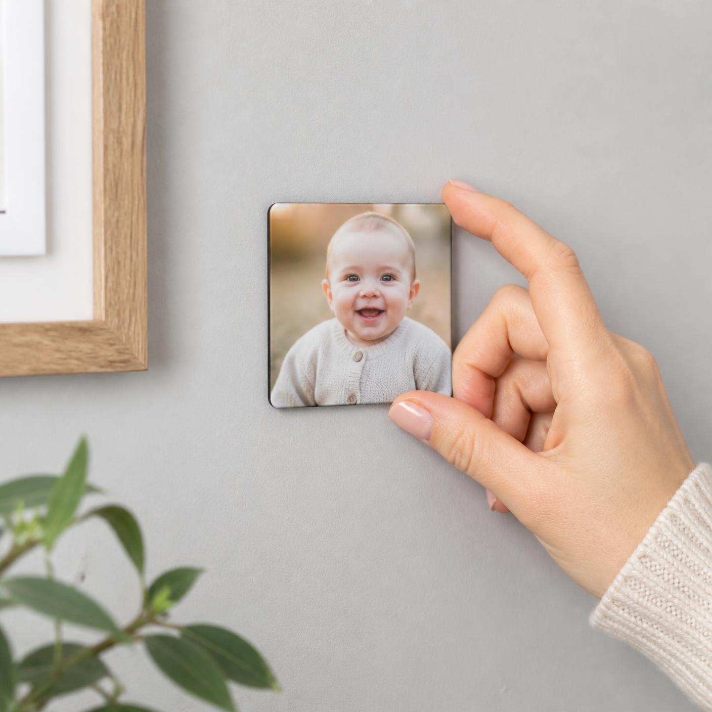 A hand placing a photo magnet of a smiling baby onto a grey wall